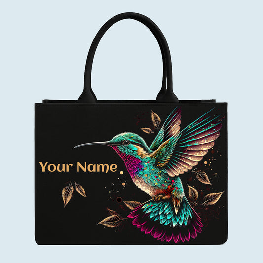Black tote bag with a colorful hummingbird design on a light blue background