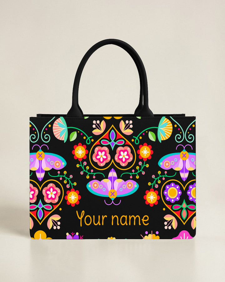Black tote bag with an abstract mosaic sun and flower design in red and blue, featuring a custom name in a vibrant coral-pink font.