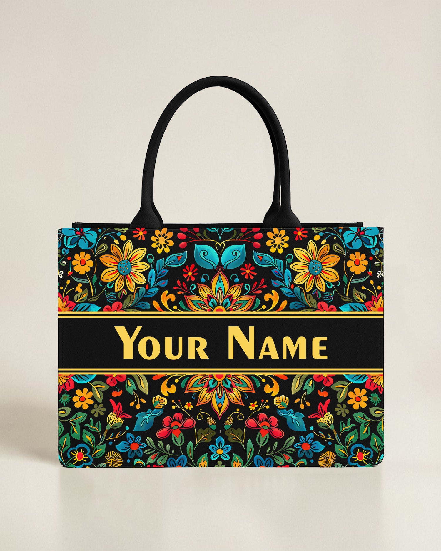 Black canvas tote bag with a geometric mosaic sun and mountain landscape in earthy red, blue, and gold tones, featuring a custom name in coral-pink font.