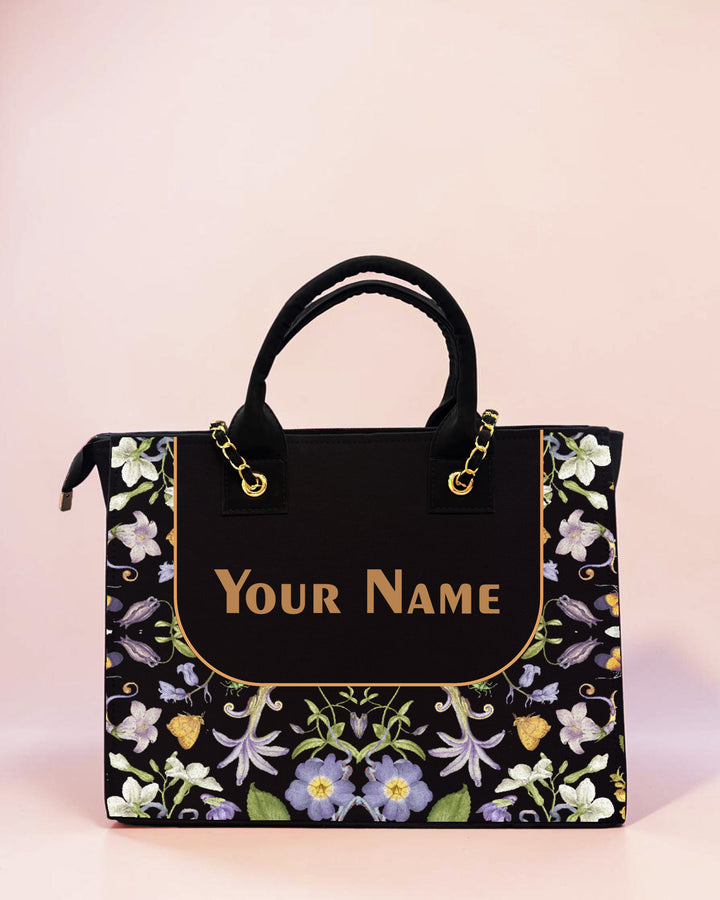 Elegant personalized black floral tote bag with custom name print, botanical flower artwork, and luxury handbag design displayed on a soft pastel background.