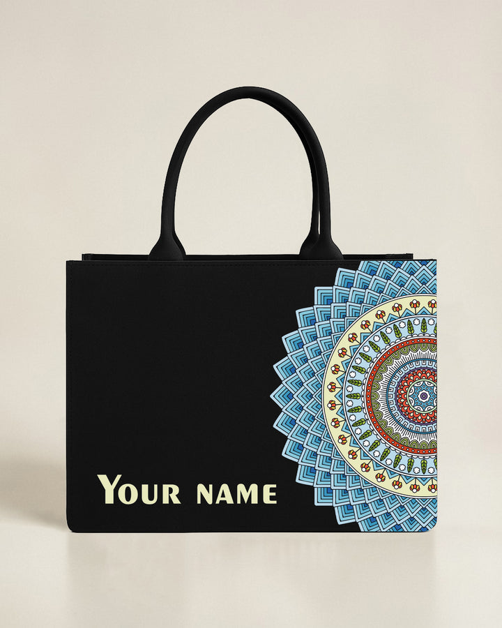 Black tote bag with a centered gold and teal celestial sun and moon mandala design, featuring a custom name in elegant gold-toned font.