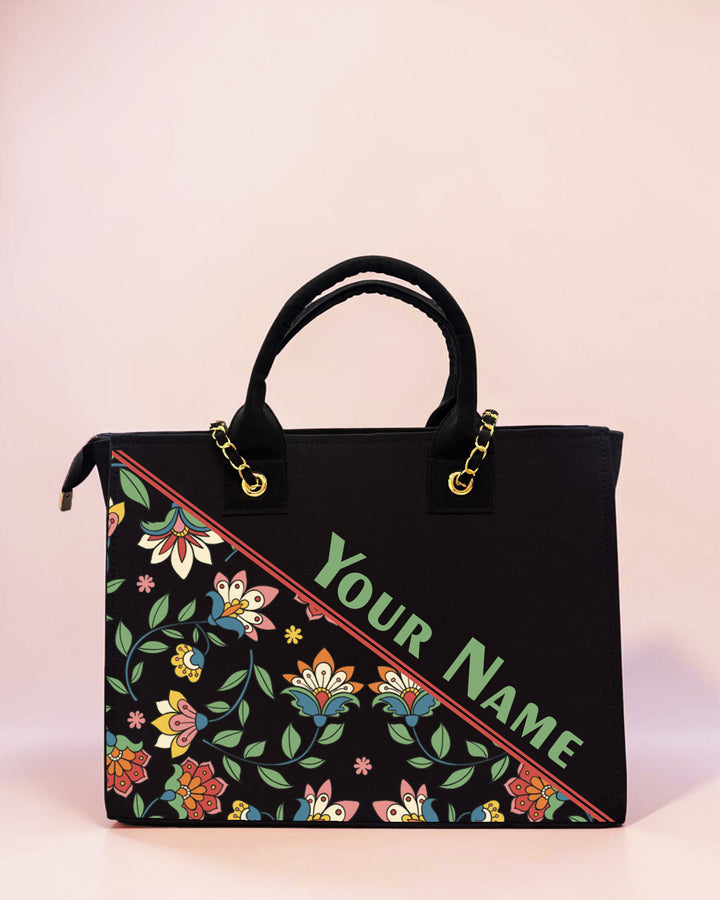 Personalized black tote bag featuring colorful ethnic floral artwork and custom name print on a pastel background.