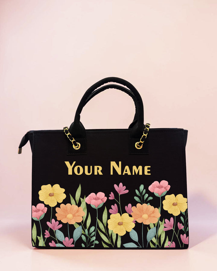 Personalized black floral tote bag with pastel flower artwork and custom name print displayed on a soft pastel background.