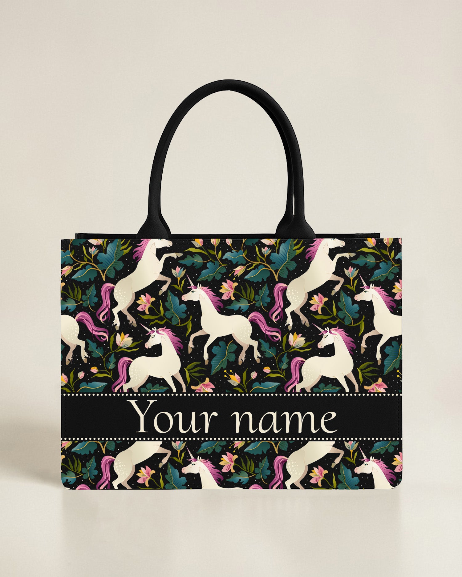 Black canvas tote bag featuring a vibrant teal hummingbird hovering over a border of pink flowers and green vines, with a custom name in bright lime-green font.